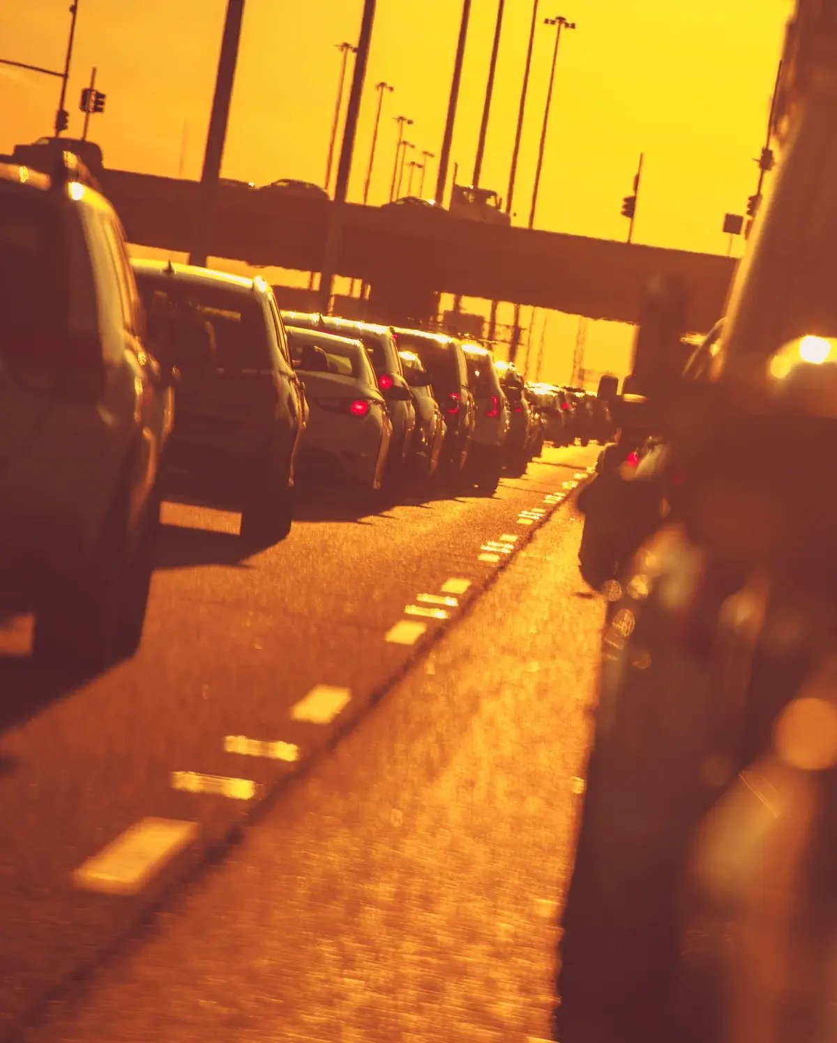 A vertical shot of heavy highway traffic jam at sunset, with car silhouettes against a warm orange glow A vertical shot of heavy highway traffic jam at sunset, with car silhouettes against a warm orange glow