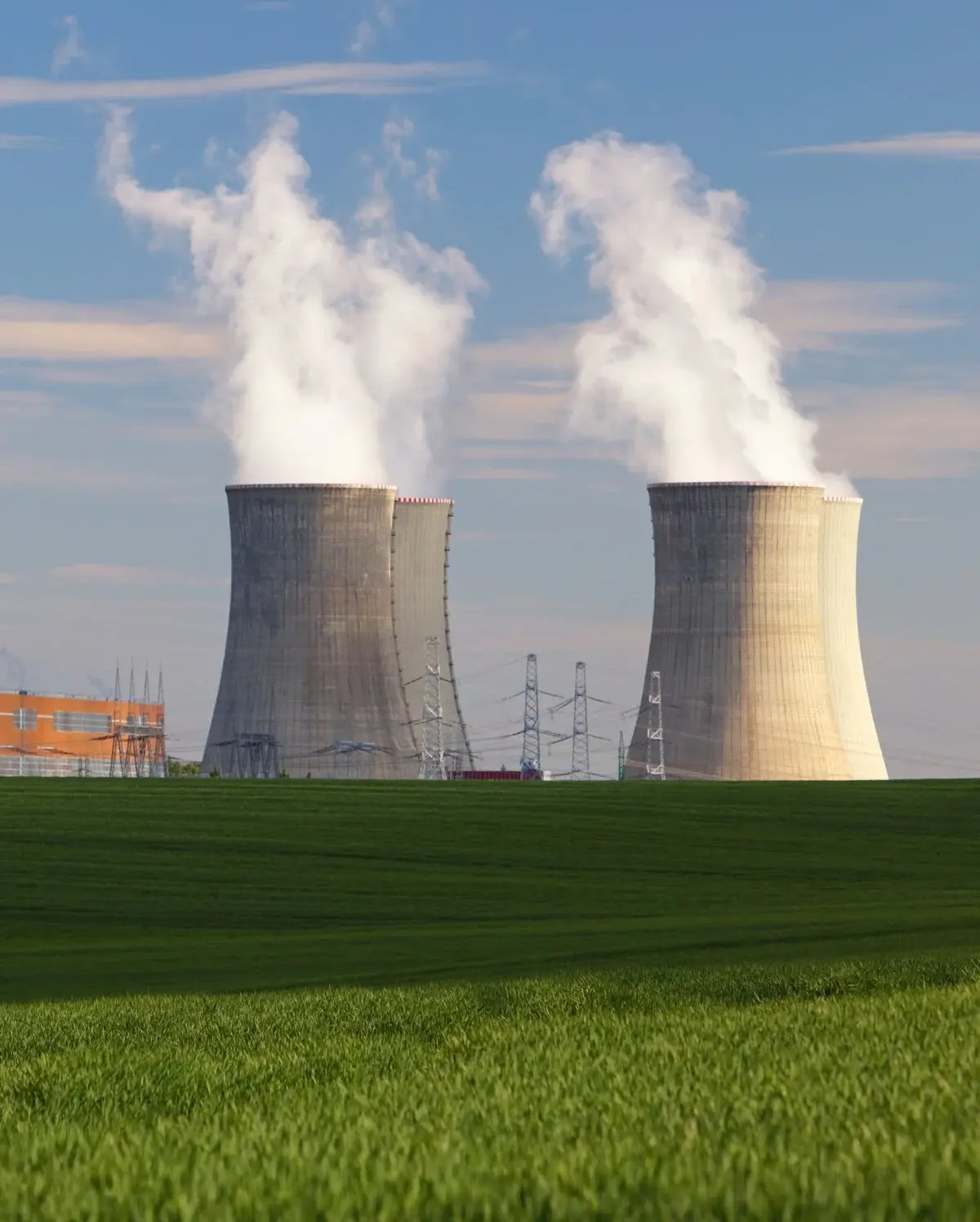 Two massive cooling towers of a nuclear power plant emitting steam, viewed from across a green field Two massive cooling towers of a nuclear power plant emitting steam, viewed from across a green field